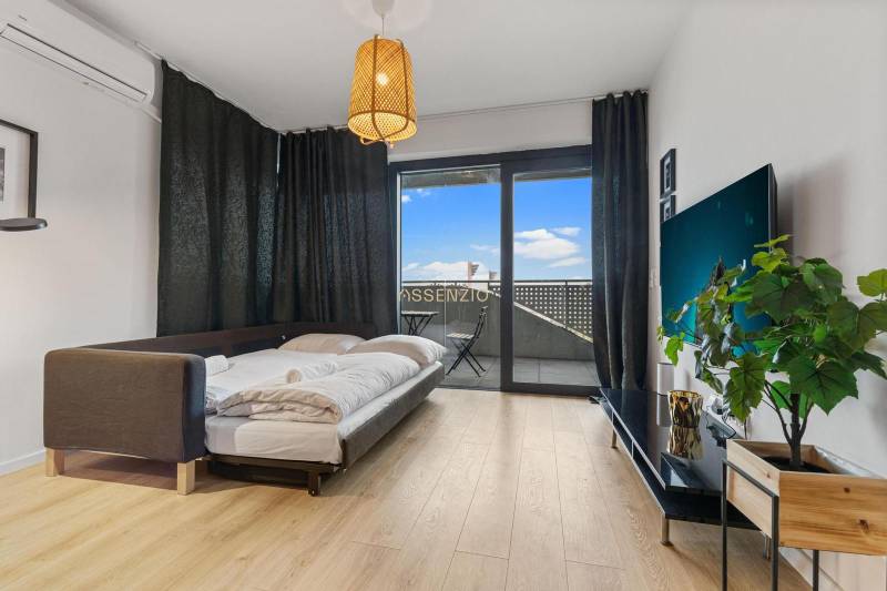 Living area in a studio apartment with a bed, wood-patterned flooring, and a balcony.