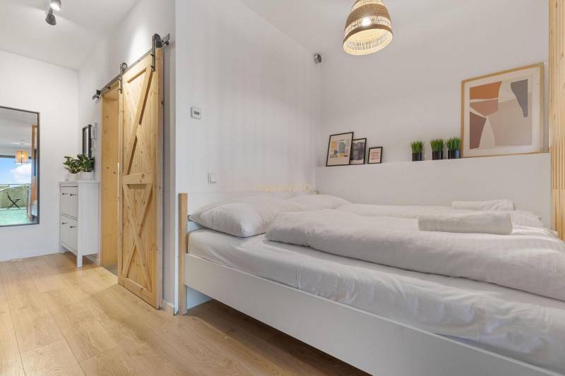 A bedroom in a studio apartment with sliding doors and a wood-patterned floor.