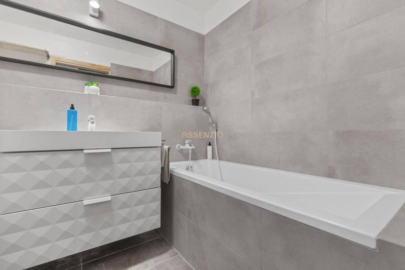 A bathroom with a bathtub, sink, and mirror in a studio apartment.