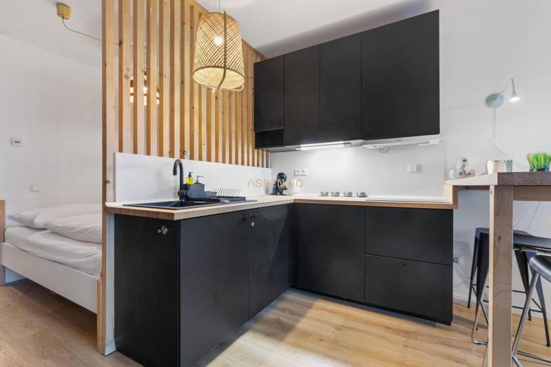 A kitchen in a studio apartment with black cabinets and a wood-patterned floor.