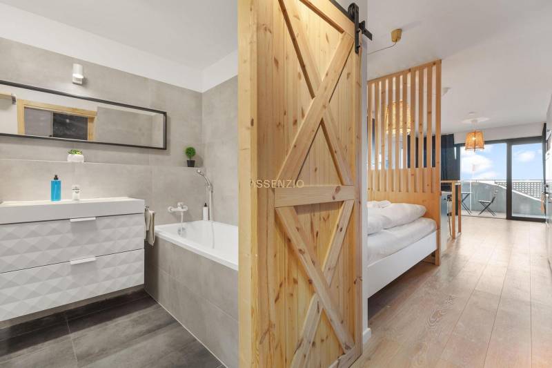 Interior of a 1-room apartment with a bathtub and a floor with a wood decor.