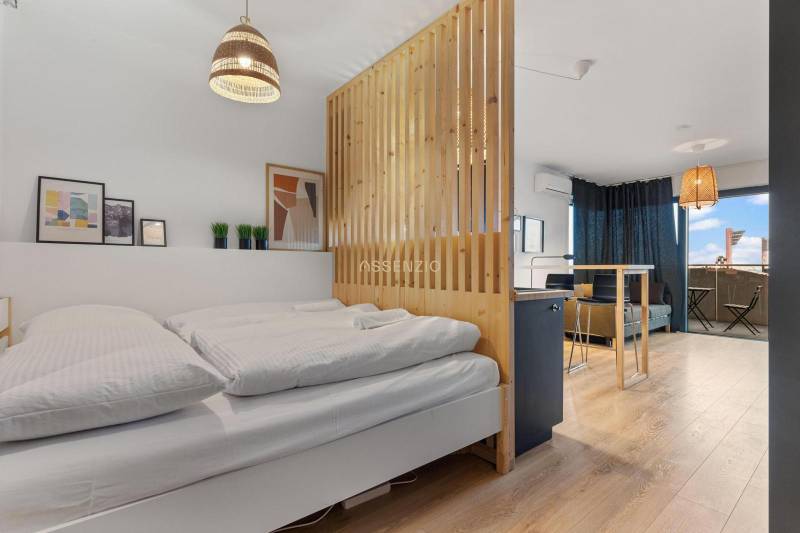 A bright room with a bed, a wooden panel, a floor with a wooden decor, and a balcony.