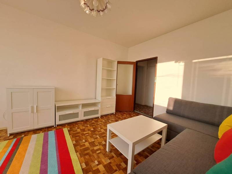 Living room with white cabinets, a gray sofa, and a wood-patterned floor in a two-room apartment.