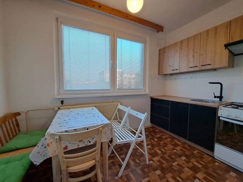 A kitchen in a 2-room apartment with a wooden decor floor and a dining area.