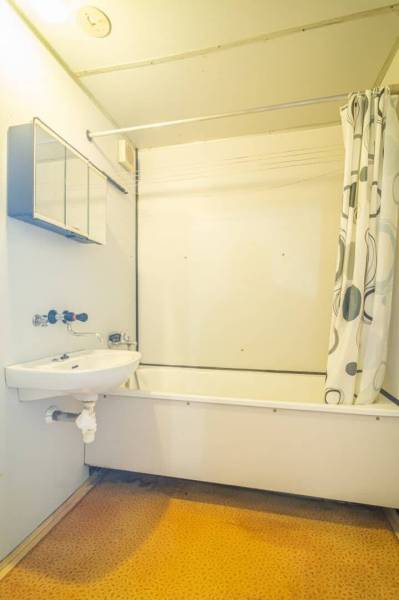 A bathroom with a bathtub and a shower curtain in a 2-room apartment, light walls, orange floor.