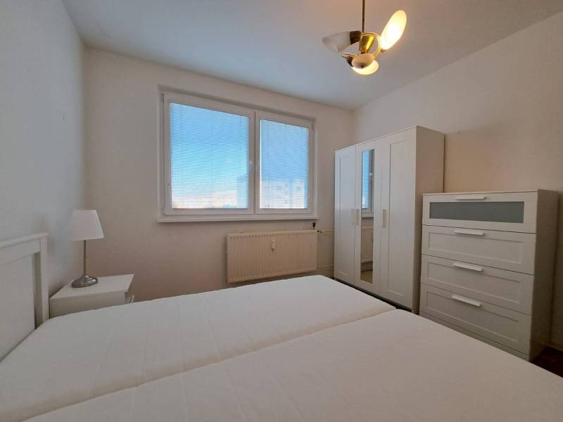 Bedroom in a two-room apartment with white furniture and a bed, window with blinds.