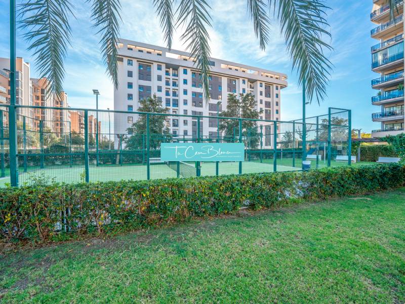 A complex of 2-bedroom apartments in Alicante with a paddle court, palm trees, and green lawn.