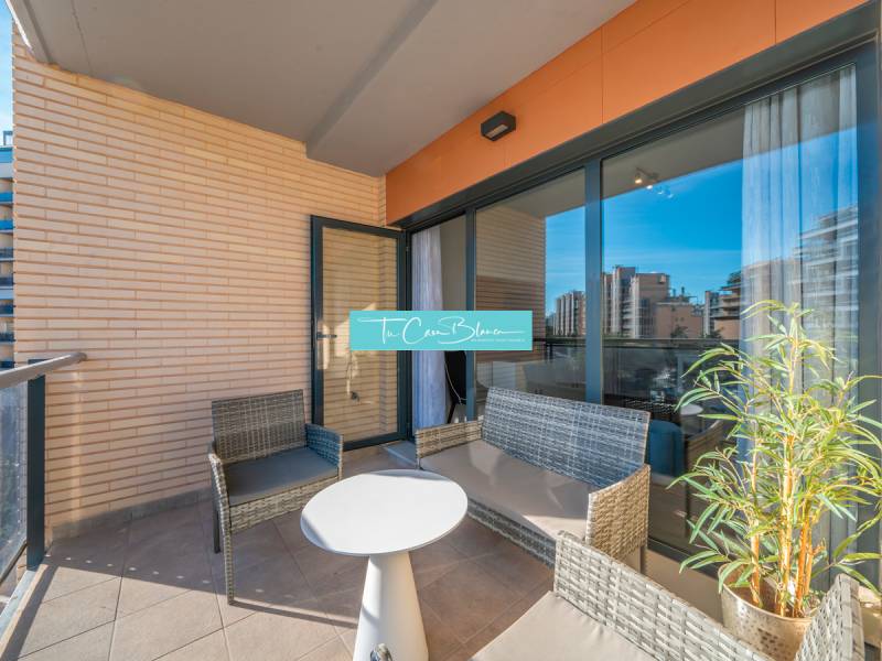 Terrace of a 2-bedroom apartment in Alicante with rattan seating and a view of the city.