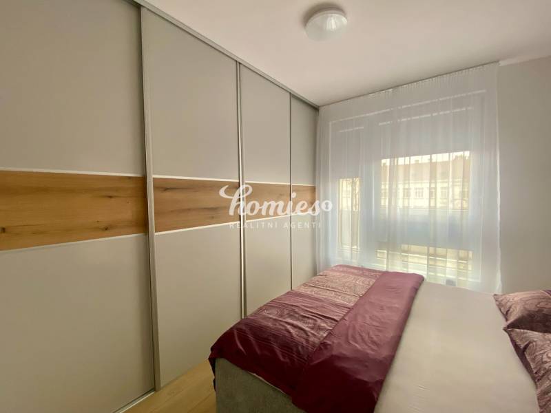 Bedroom in a 2-room apartment with a large wardrobe and a bed, wooden decor flooring.