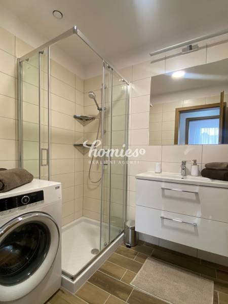 Bathroom in a 2-room apartment with a washing machine, shower corner, and floor with wood decor.