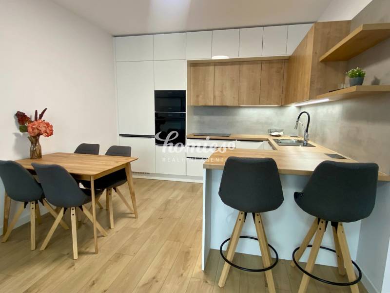 A kitchen in a 2-room apartment with a wooden decor floor, a dining table, and a bar counter.