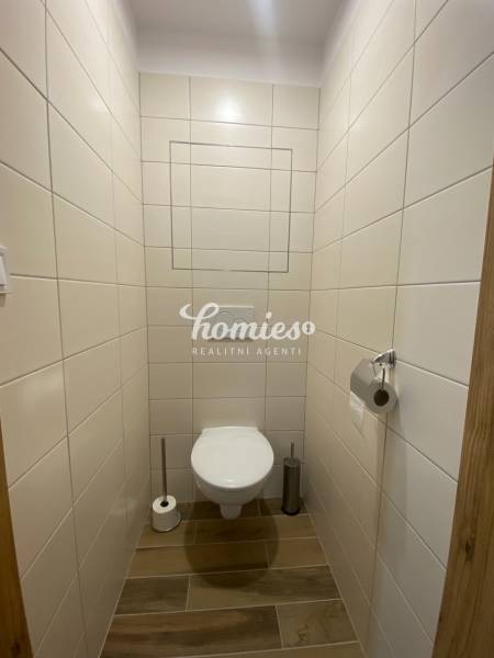 A toilet with wooden decor tiles and flooring in a 2-room apartment.