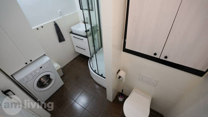 Bathroom with a washing machine, shower, and toilet in a 3-room apartment.