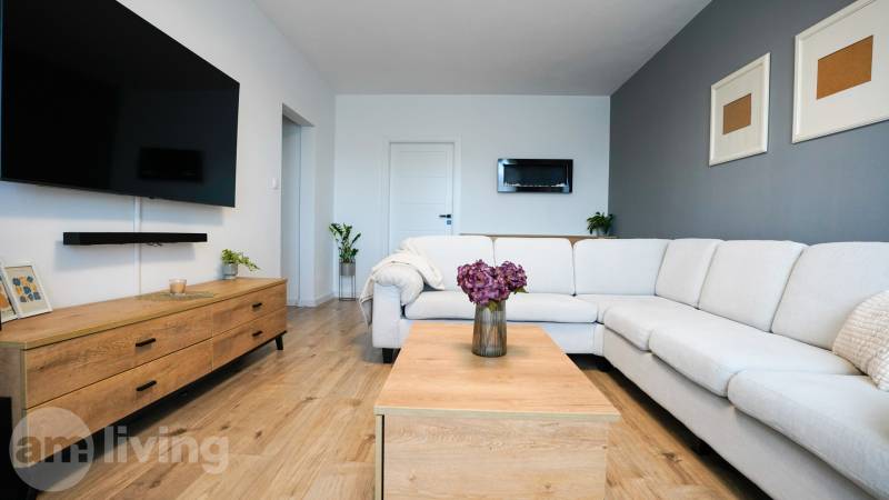 Living room in a 3-room apartment with a white couch, wood-patterned flooring, and decorations.