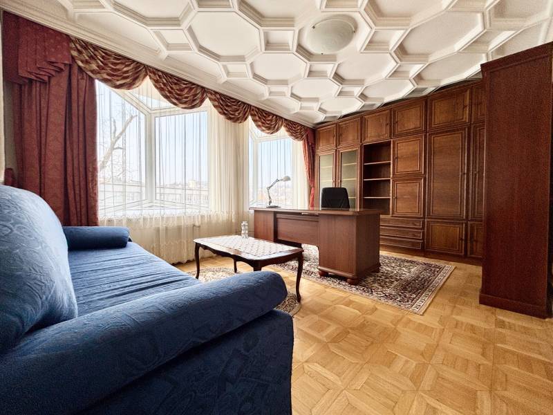 A room in a 4-room apartment with a comfortable sofa, a work desk, and a floor with a wooden decor.