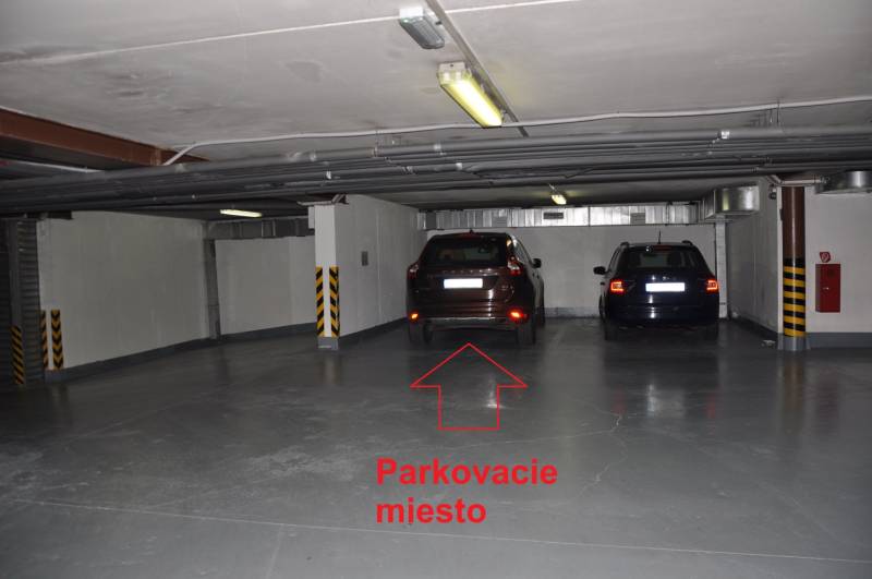 Underground garage with parked cars and a free parking spot marked with a red arrow.