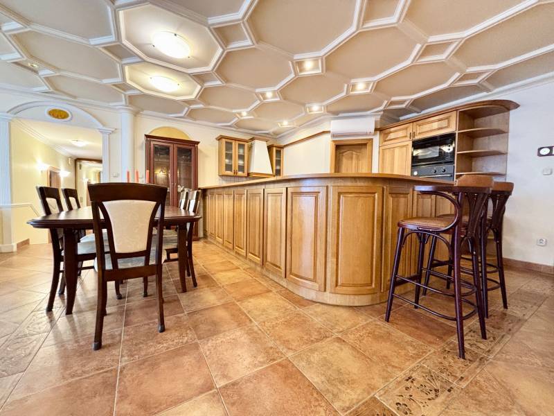 A kitchen in a 4-room apartment with a dining table, wooden furniture, tiles, and an interesting ceiling.
