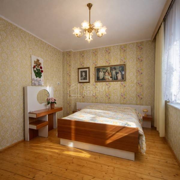 A bedroom in a family house with a wood-patterned floor and floral wallpaper.
