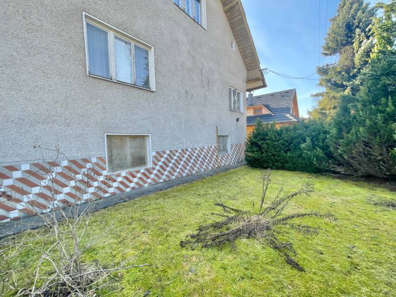 A family house in Terchová with a grassy plot, surrounded by shrubs and decorative cladding.