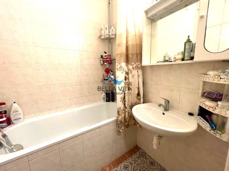 Bathroom in a studio apartment with a bathtub, mirror, and tiles on the walls.