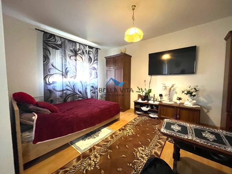 A one-room apartment with a bed, a television, and a floor with a wooden decor.