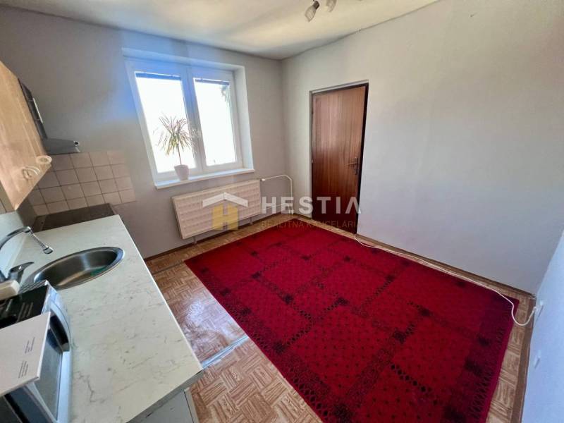 The kitchen of a three-room apartment with carpet, wooden decor flooring, and simple furnishings.