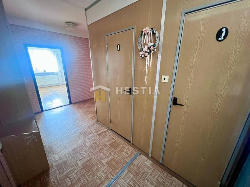 A hallway in a 3-room apartment with a wooden decor floor and a decorative wreath on the door.