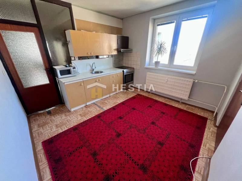 A kitchen in a 3-room apartment with a wooden decor floor and a red carpet.