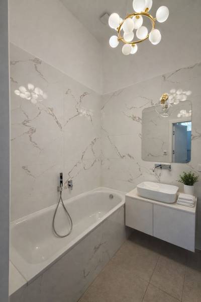A bathroom with a bathtub, sink, mirror, and decorative light fixture in a 3-room apartment.