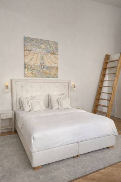 Bright bedroom with a bed, painting on the wall, nightstand, and wood-patterned floor.