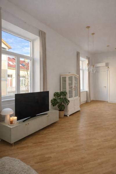 Living room in a 3-room apartment with wood-patterned flooring, a television, and large windows.