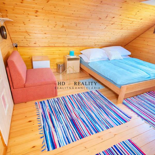 Attic cabin with a bed, sofa, wooden decor flooring, and striped carpet.