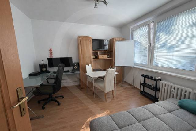 Interior of a 3-room apartment with a wooden decor floor, a desk, and a sofa.