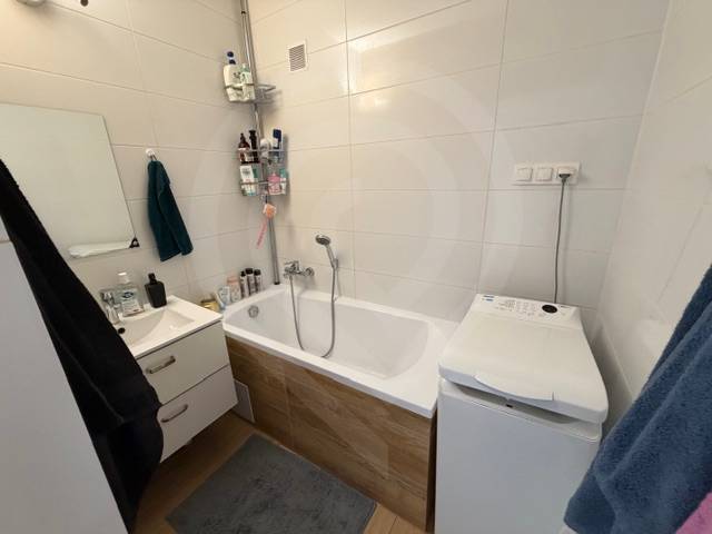 Bathroom in a 3-room apartment with a bathtub, sink, and washing machine, white tiles.