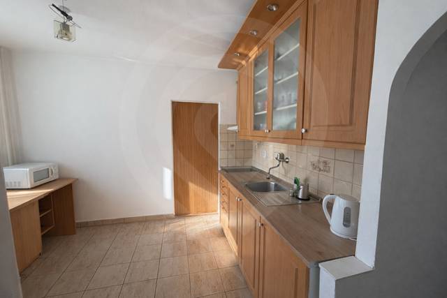 A kitchen in a 3-room apartment with wooden cabinets and white appliances on tiles.