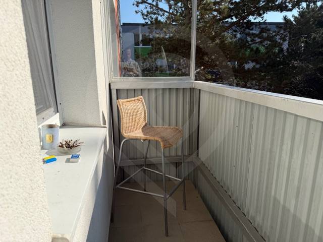 A balcony in a 3-room apartment with a bar stool and items on the windowsill.