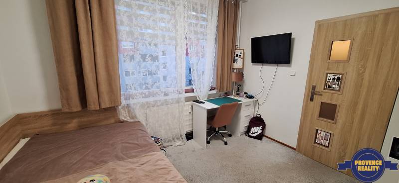 A room in a 4-room apartment with a table, bed, and television, floor with wooden decor.