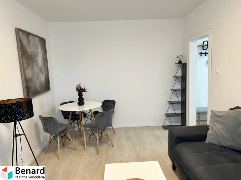 Living room in a two-room apartment with a wooden decor floor, gray sofa, and dining table.