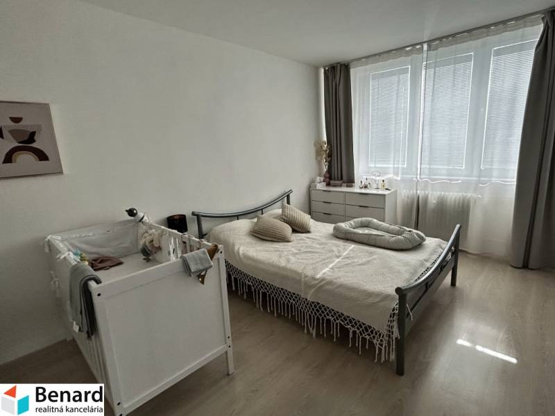 Bedroom in a 2-room apartment with a crib, bed, and dresser, floor with wooden decor.