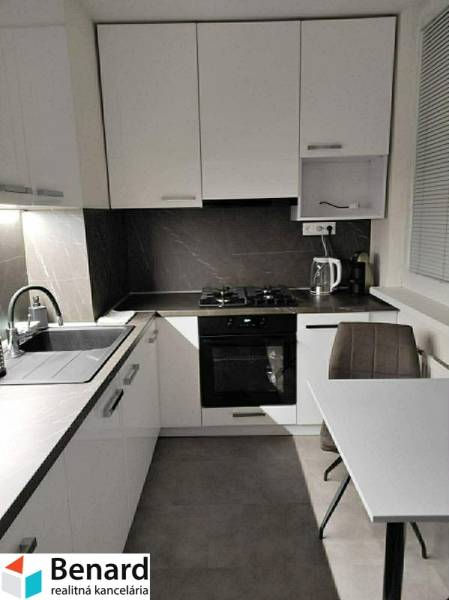 A kitchen with white cabinets and a table in a two-room apartment with a wood-patterned floor.