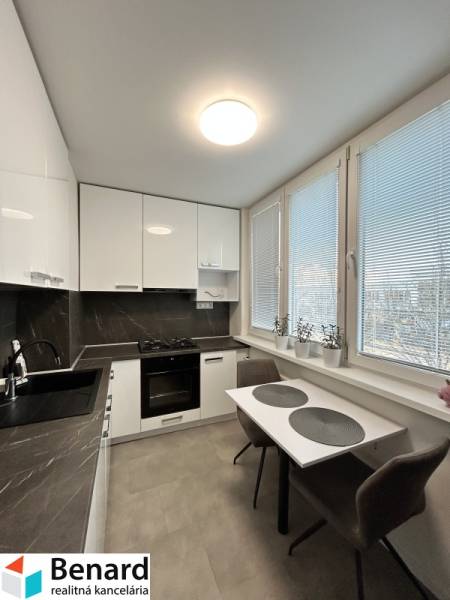 A kitchen in a 2-room apartment with white furniture and a dark countertop.