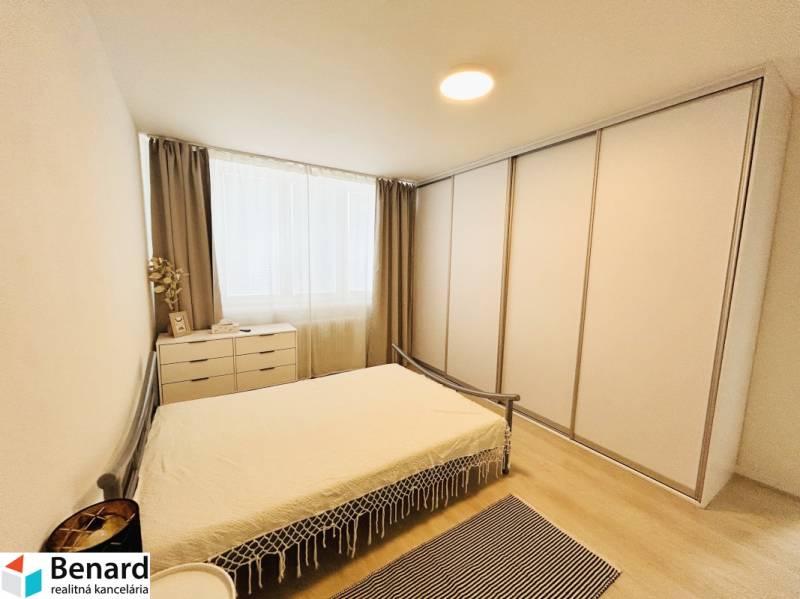Bedroom in a 2-room apartment with wood-patterned flooring, a large wardrobe, and a drawer chest.