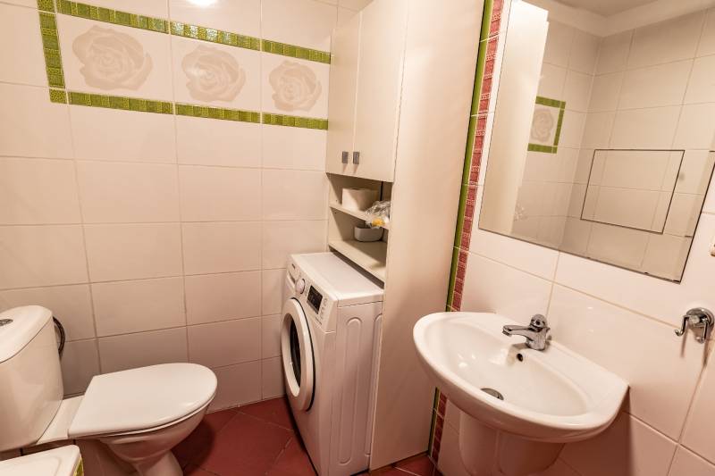 Bathroom in a 2-room apartment with a washing machine, sink, and toilet, tiled with white tiles.
