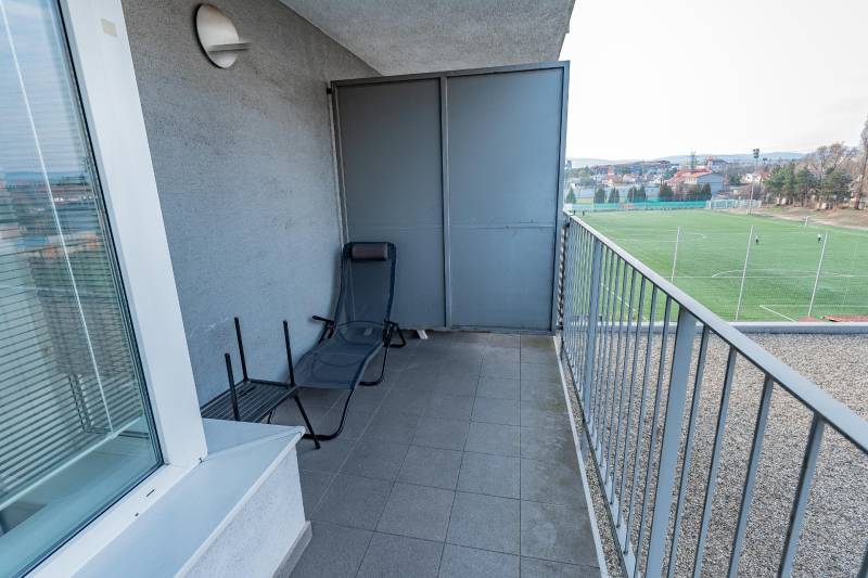 A balcony of a 2-room apartment with a view of the football field and a lounger.