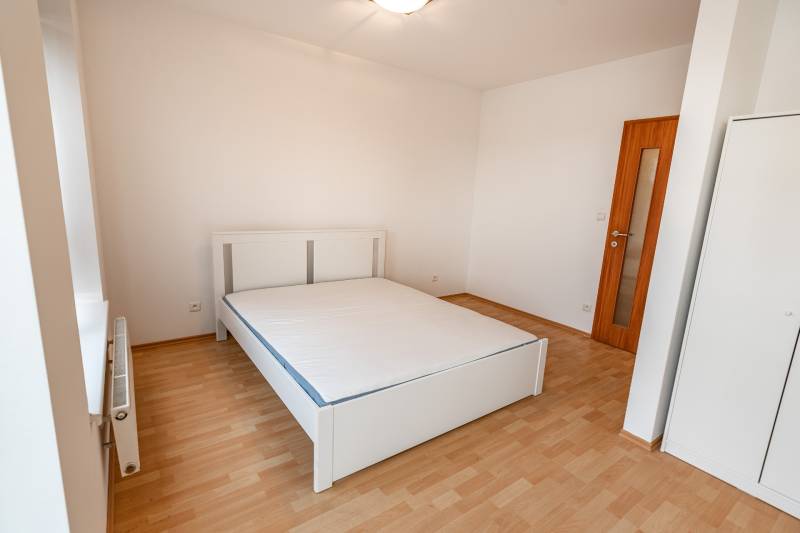 A bedroom in a two-room apartment with a white bed and a wooden decor floor.