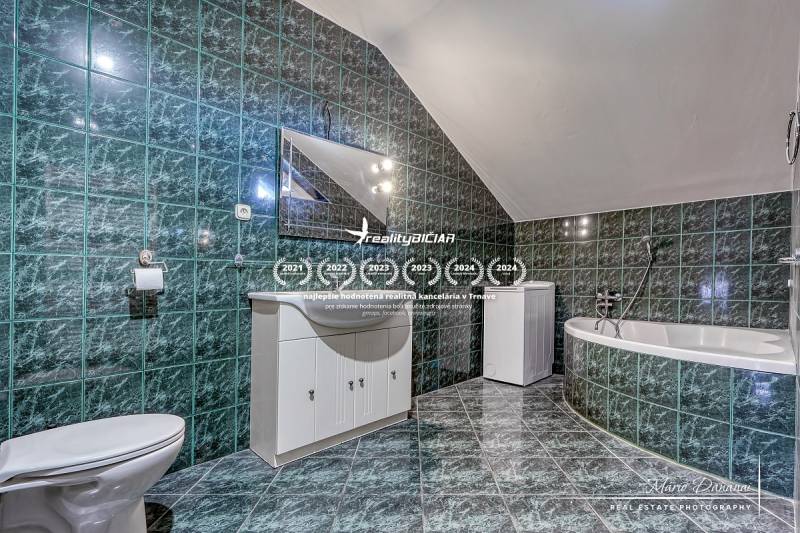A bathroom in a family house with a bathtub, green tiles, and white furniture.