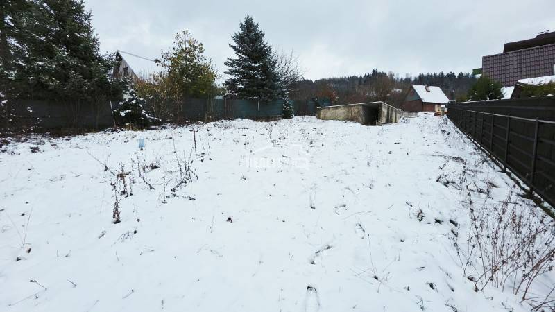 Snow-covered recreational plots in Považská Bystrica with a view of the forest and house.