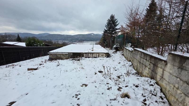 Snow-covered recreational plots in Považská Bystrica with a view of the mountains and planted trees.