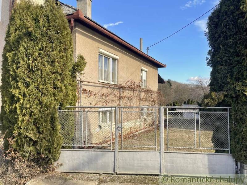 A family house in Bretka with a living hedge and a metal gate on a fenced plot.