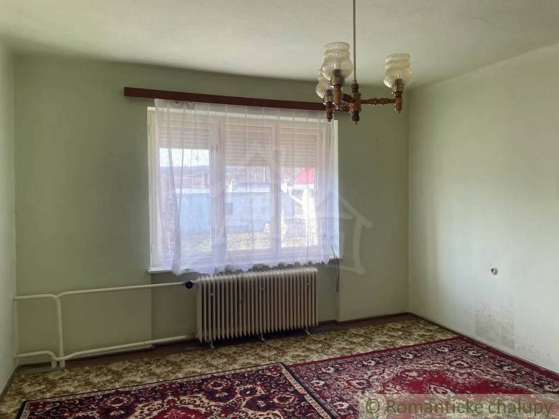 A room in a family house with a radiator, carpet, and curtains on the window.